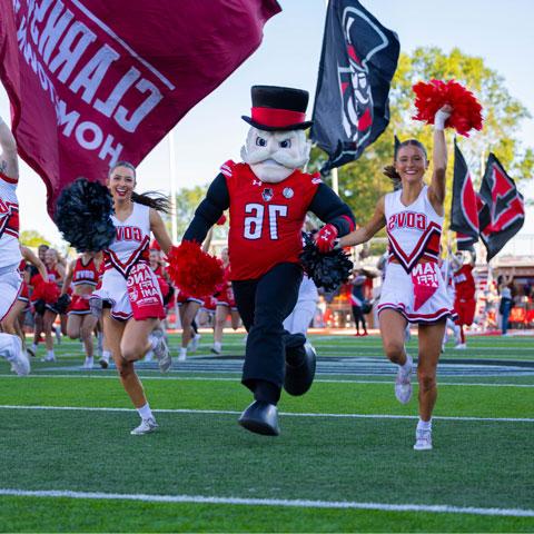 The gov running on football field with cheerleaders